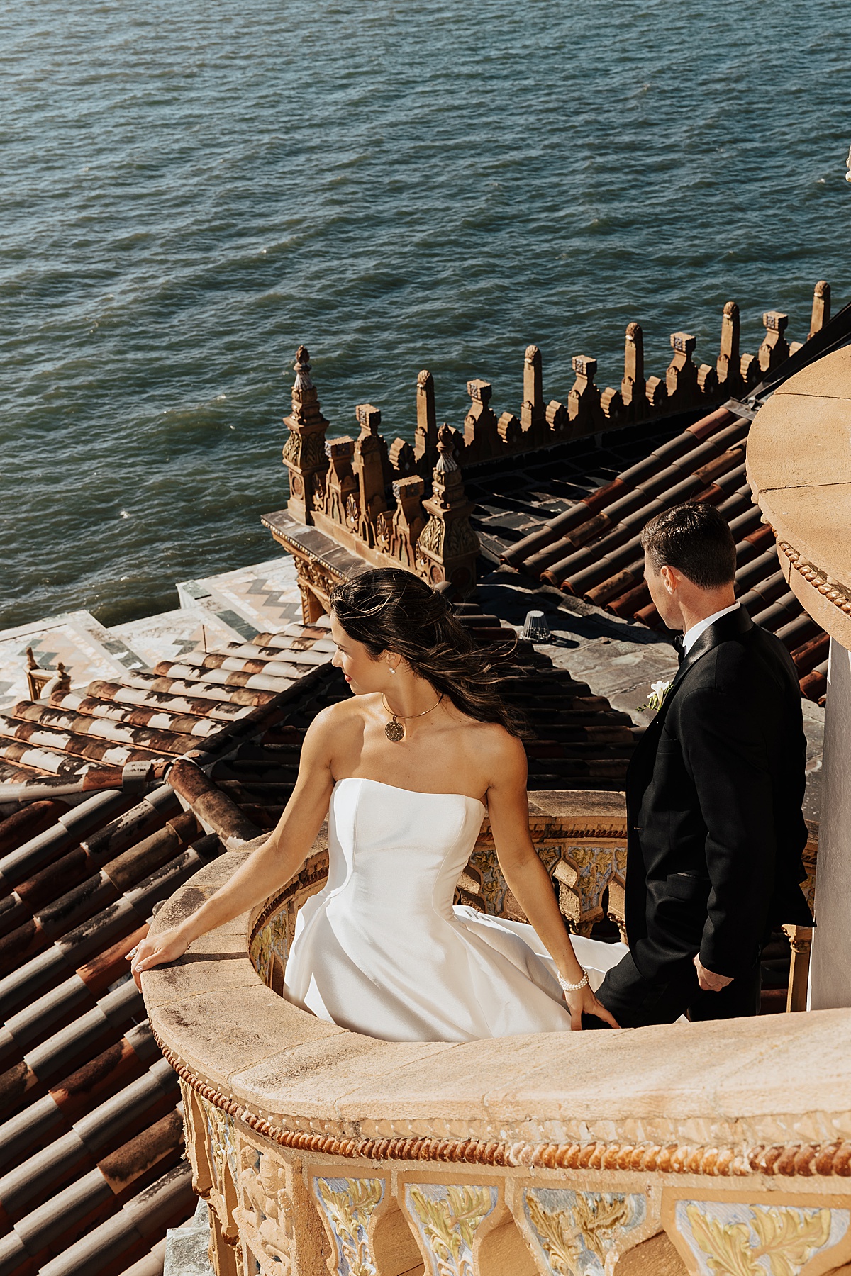 Bride and groom stand on stairwell and peer out at the ocean by Florida wedding photographer